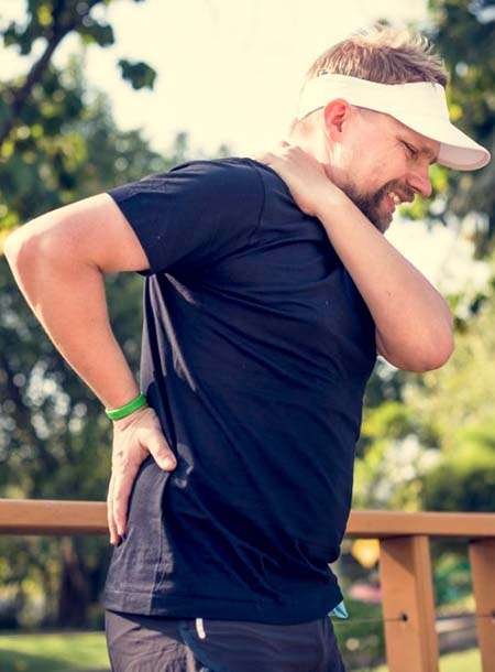 Man in pain holding neck and lower back outdoors