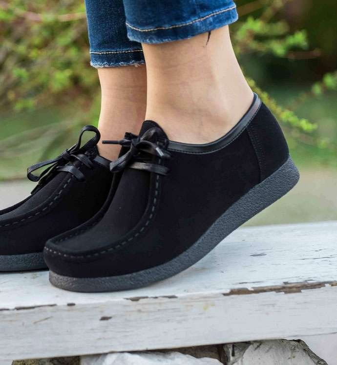 Black casual shoes on person standing on wooden ledge