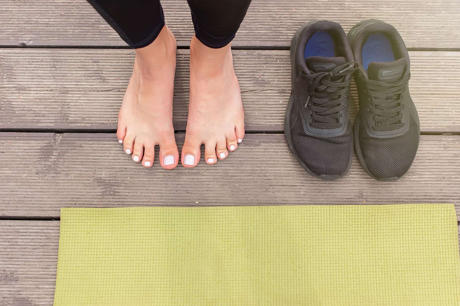 Bare feet beside sneakers on wooden floor near yoga mat