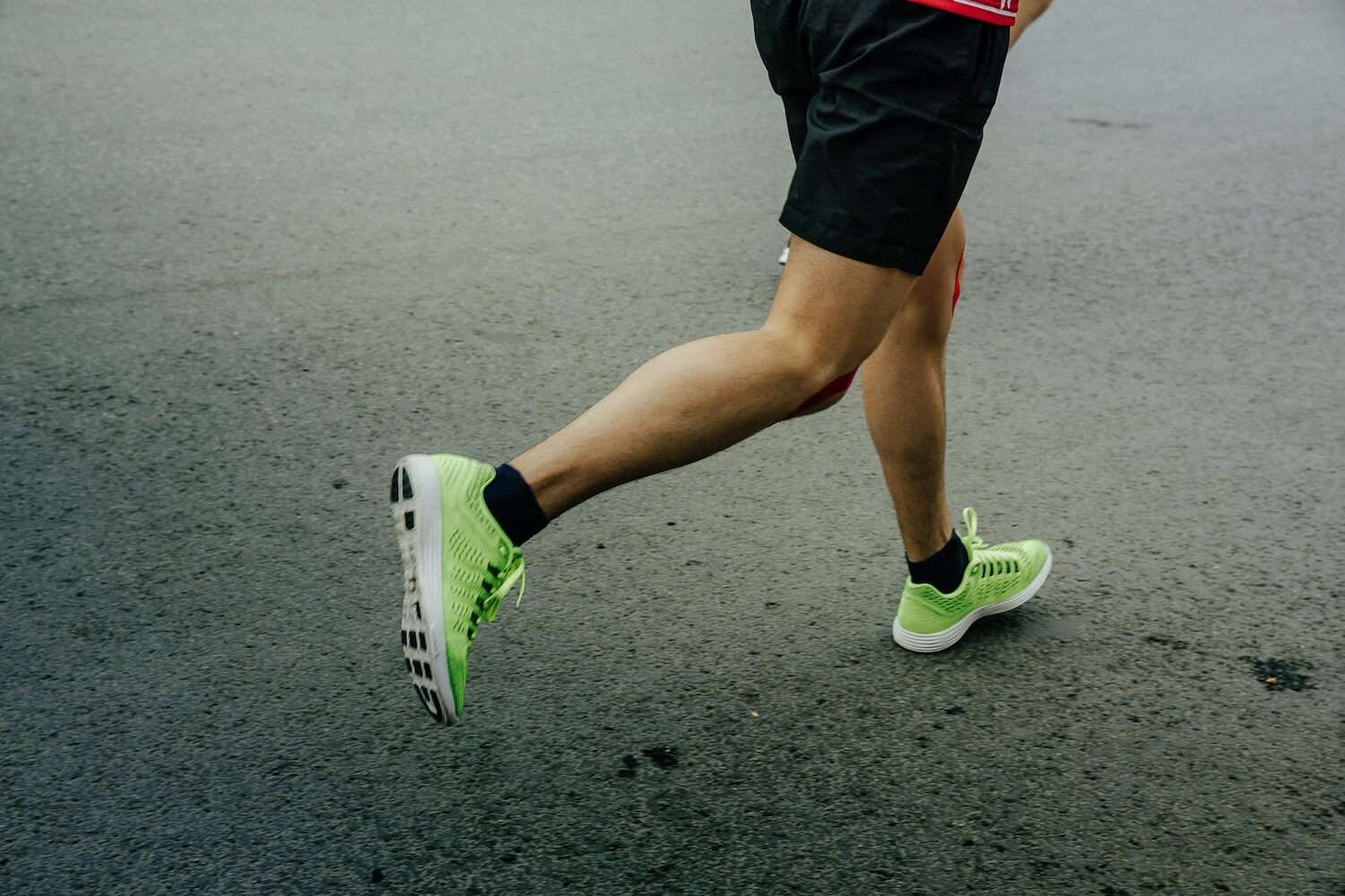 Runner in motion wearing green shoes on asphalt