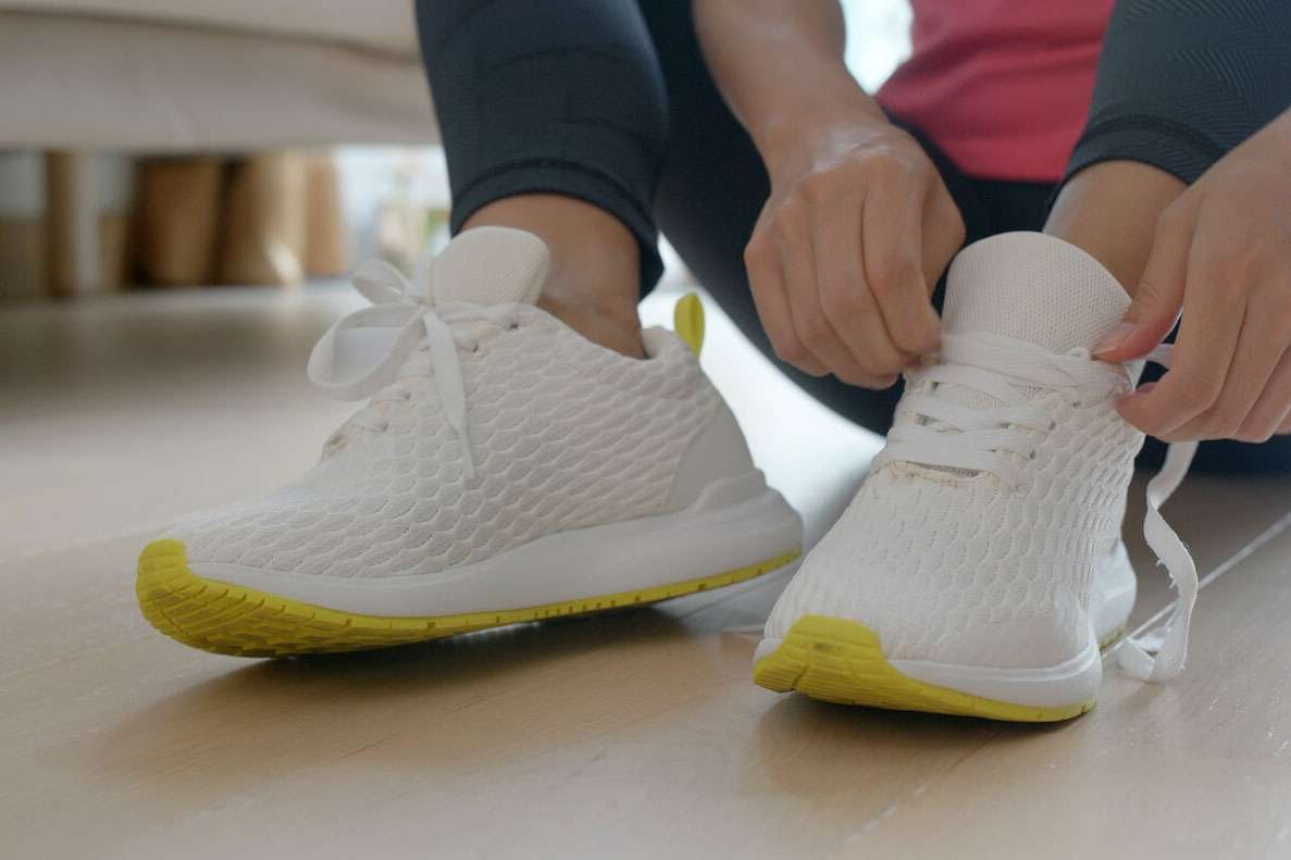 Person tying white running shoes with yellow soles